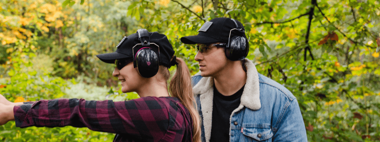 Man and woman wearing TradeSmart Safety earmuffs and protective glasses during outdoor shooting practice in the woods.
